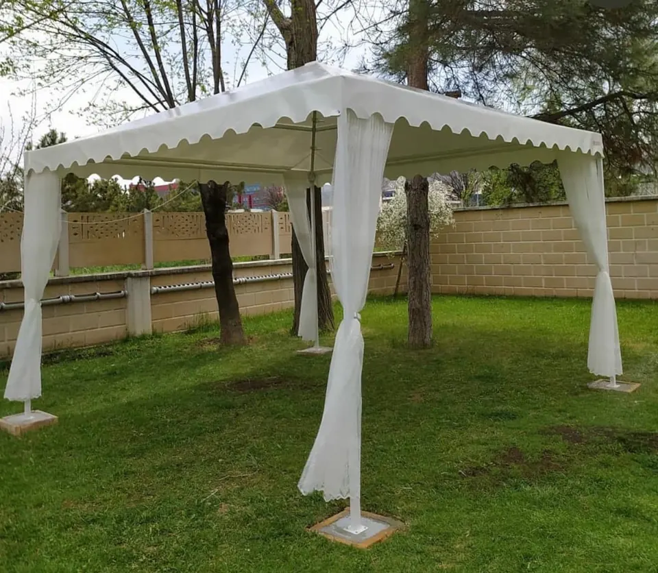 Çim bahçeye kurulan beyaz dalgalı saçaklı gazebo çadır ve köşelerde tül perdeler