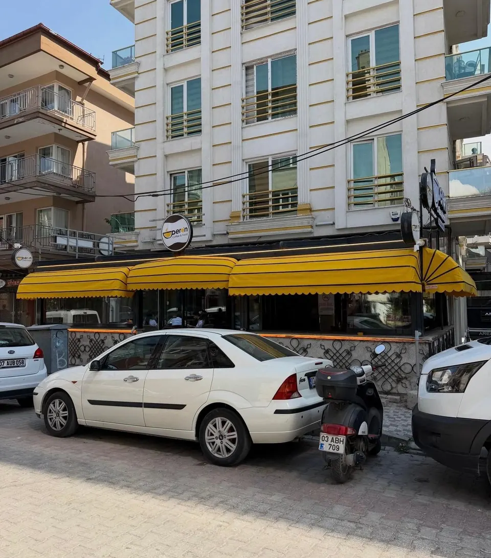 Köşe binadaki kafe cephesi boyunca siyah şeritli sarı körüklü tente ve yelpaze köşe parçası