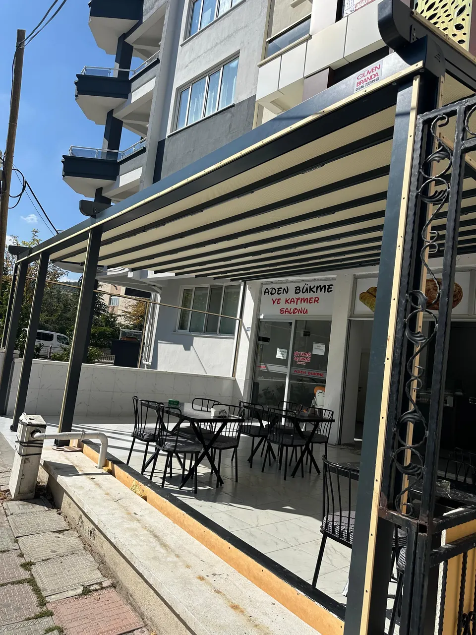 Siyah alüminyum taşıyıcılı pergole tente ile gölgelendirilmiş kafe önü