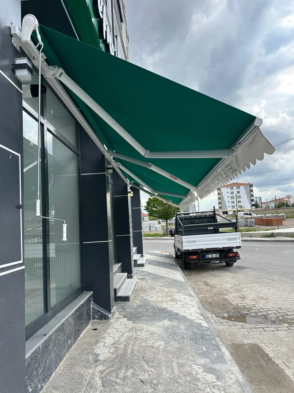 Açık konumdaki mafsallı tentenin alüminyum kolları, kasası ve manuel çevirme kolu