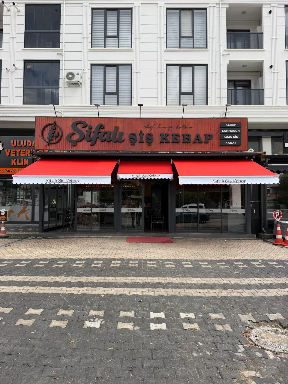 Restoran cephesi boyunca yan yana üç adet kırmızı mafsallı tente